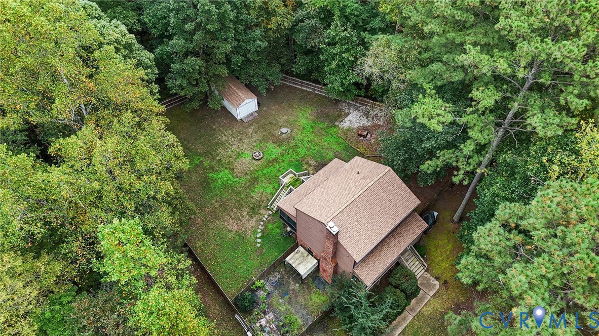 Spacious backyard featuring a detached storage shed, exterior brick chimney, stone-paver patio, and partial perimeter fencing, all surrounded by mature trees