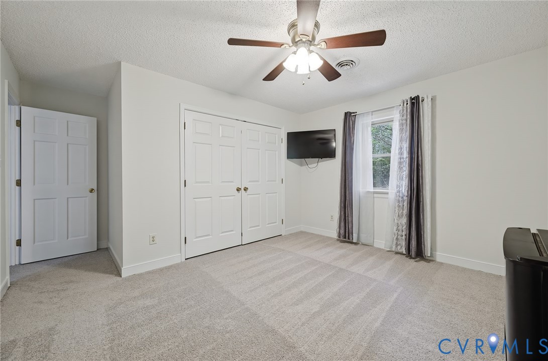 Neutral-toned wall-to-wall carpeting, ceiling fan with integrated lighting, and dual-panel closet doors