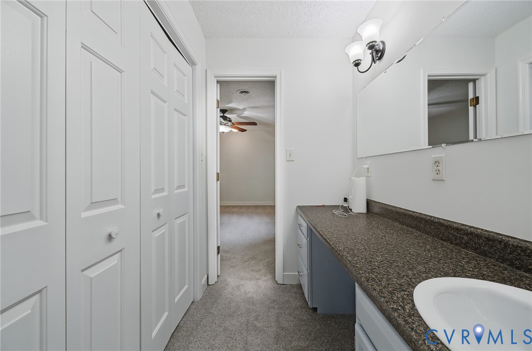 Vanity area featuring a stone-patterned countertop, integrated basin, wall-mounted dual-light fixture, expansive mirror, and white paneled bi-fold closet doors