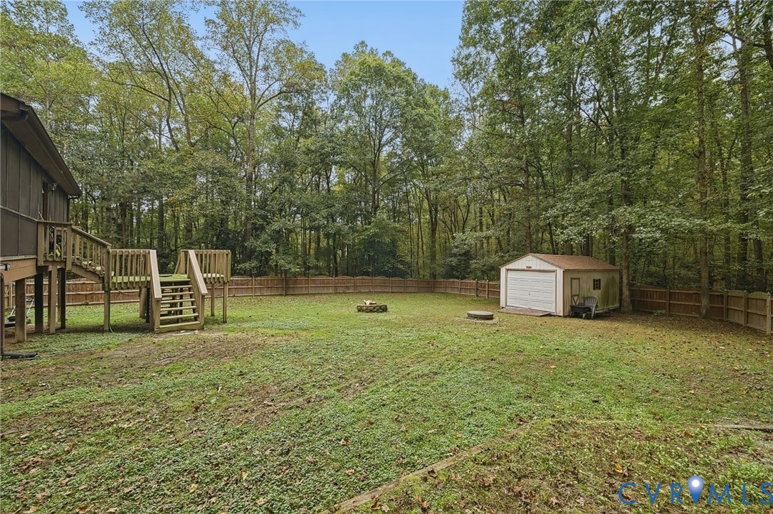 Expansive backyard featuring a wood deck, perimeter wood fencing, a detached storage shed, and mature trees