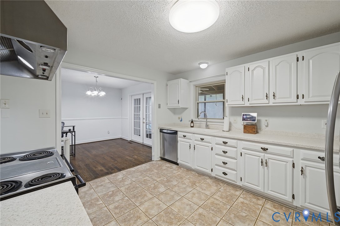 Kitchen featuring white cabinetry, solid-surface countertops, stainless steel dishwasher, and ceramic tile flooring