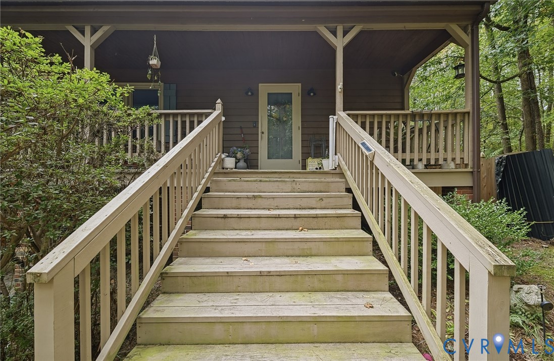 Covered front porch featuring wood decking and railings with exterior light fixtures and a glass-paneled entry door