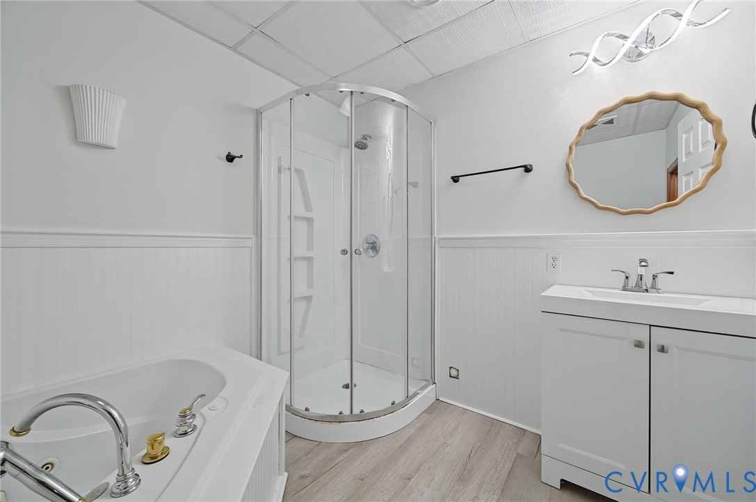 Bathroom featuring a curved corner shower, a jetted soaking tub with chrome fixtures, a white vanity with an integrated sink, and wood-finish flooring