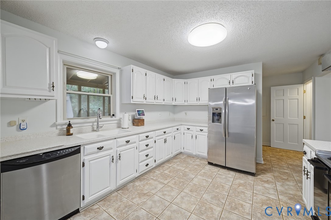 Kitchen featuring white shaker-style cabinetry, solid-surface countertops, stainless steel appliances, and ceramic tile flooring