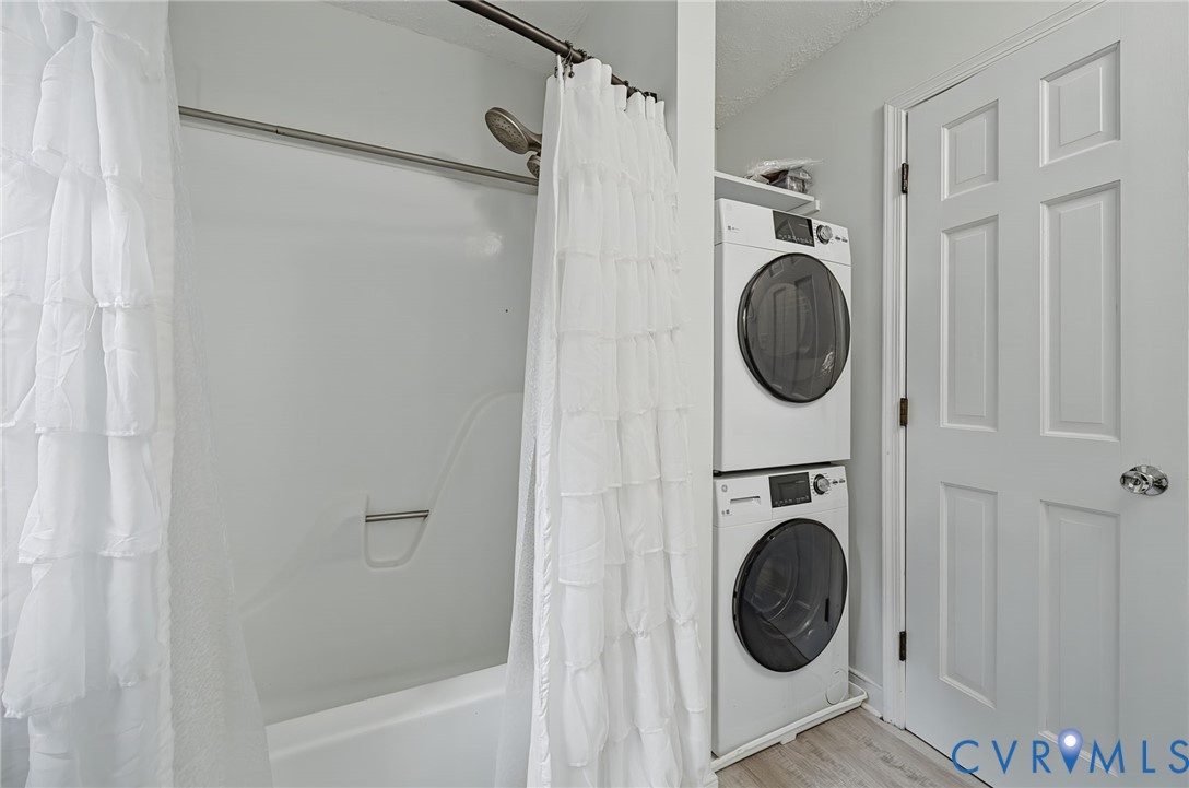Integrated laundry area featuring a stacked washer and dryer unit, shower and tub combination with a molded surround, and a paneled interior door