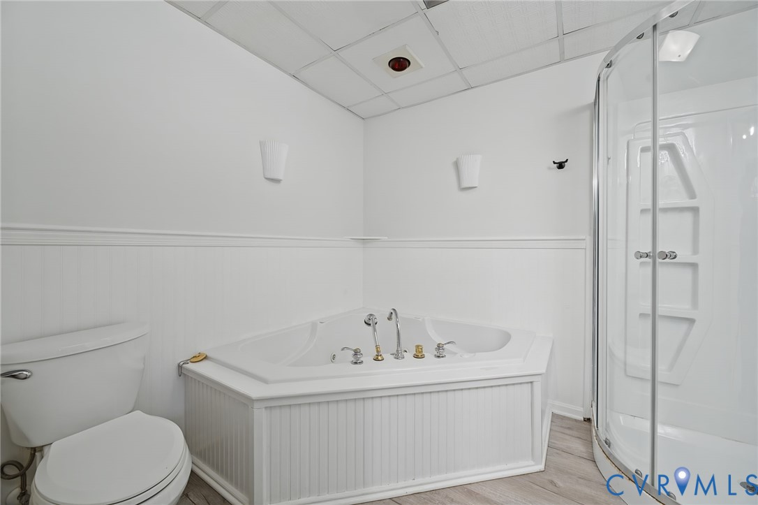 Corner soaking tub with beadboard surround, walk-in shower with curved glass enclosure, and wood-finish flooring
