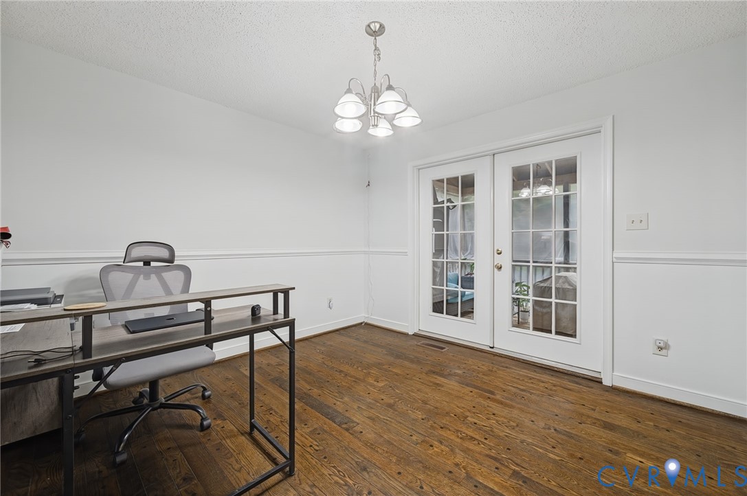 Interior space featuring wood-finish flooring, chair rail molding, a five-arm chandelier, and white-paned French doors