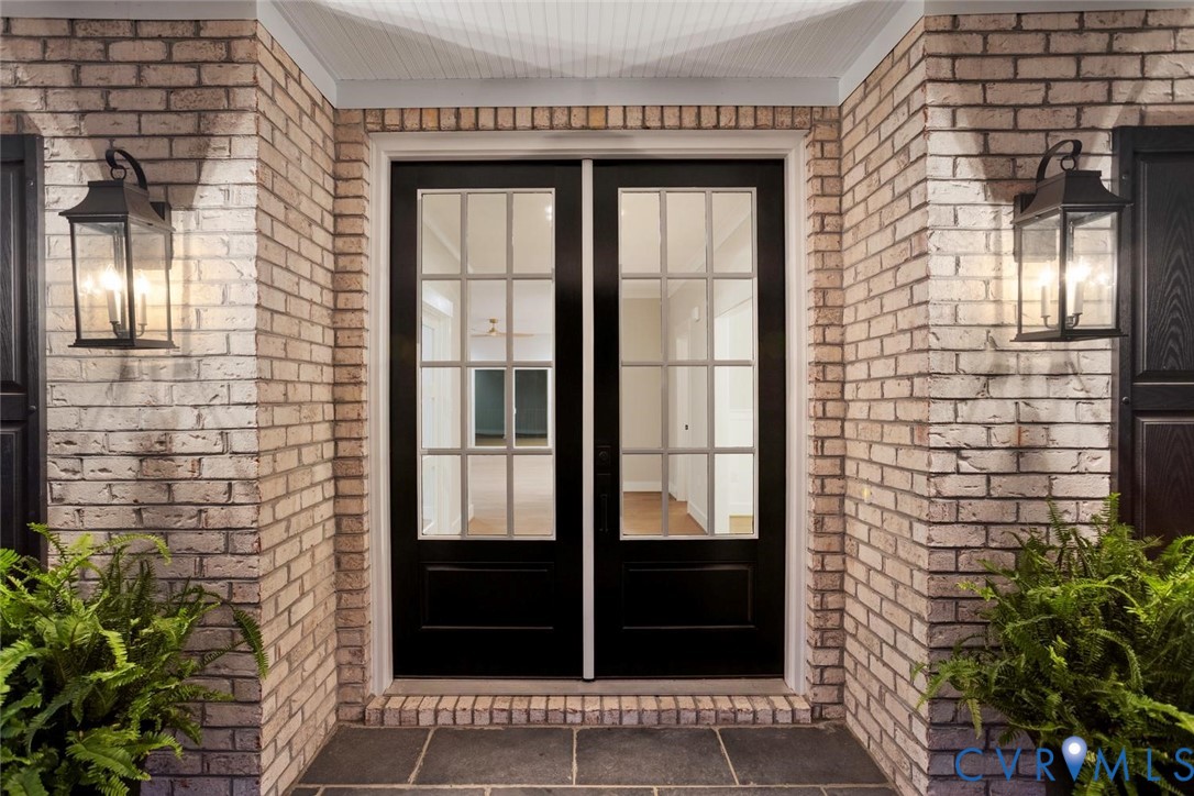 Exterior entrance featuring light brick masonry, double glass-paneled doors with grid detailing, and two wall-mounted metal lanterns