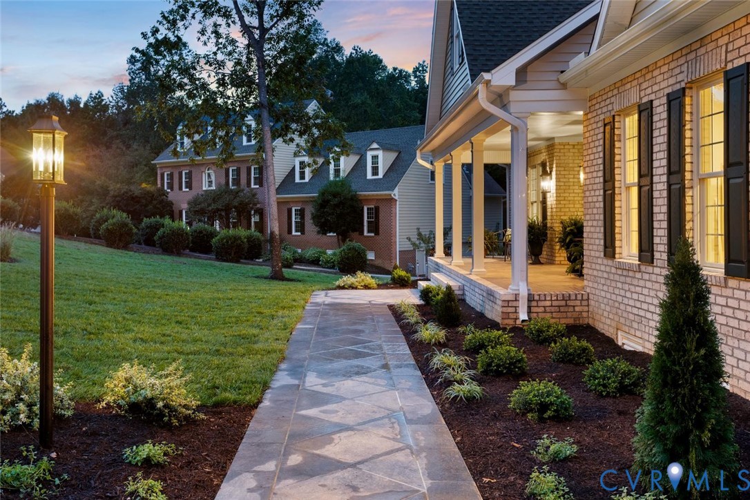 Brick exterior with decorative shutters, covered porch with column supports, stone-finish walkway, and extensive landscaping