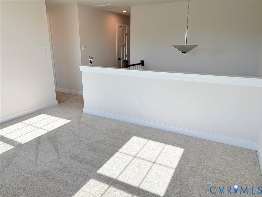 Neutral wall-to-wall carpeting, half-wall partition with white trim, and a contemporary pendant light fixture