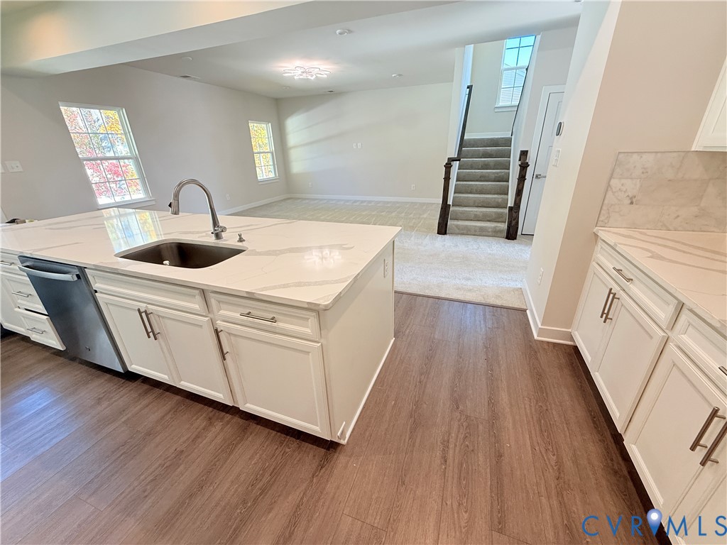 Kitchen featuring a center island with a stone-finish countertop and an under-mount sink, white cabinetry with silver-tone hardware, wood-finish flooring, and a stone-finish tile backsplash