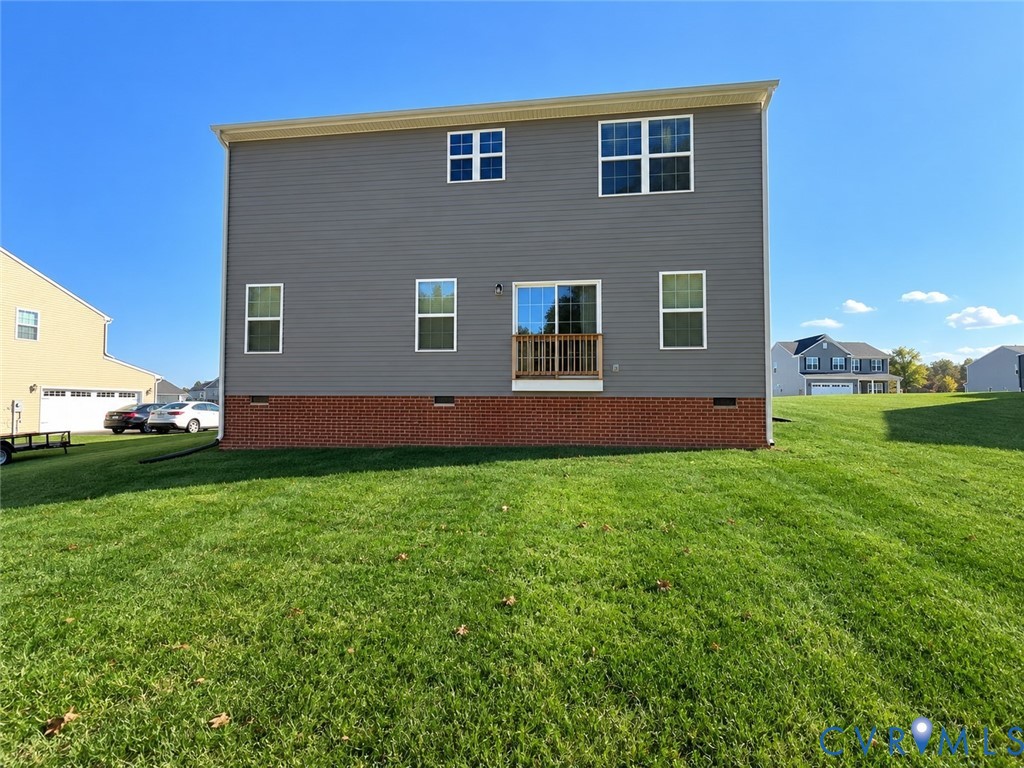Rear exterior featuring gray horizontal siding, red brick foundation, sliding glass door with a wood railing, and an expansive grass lawn