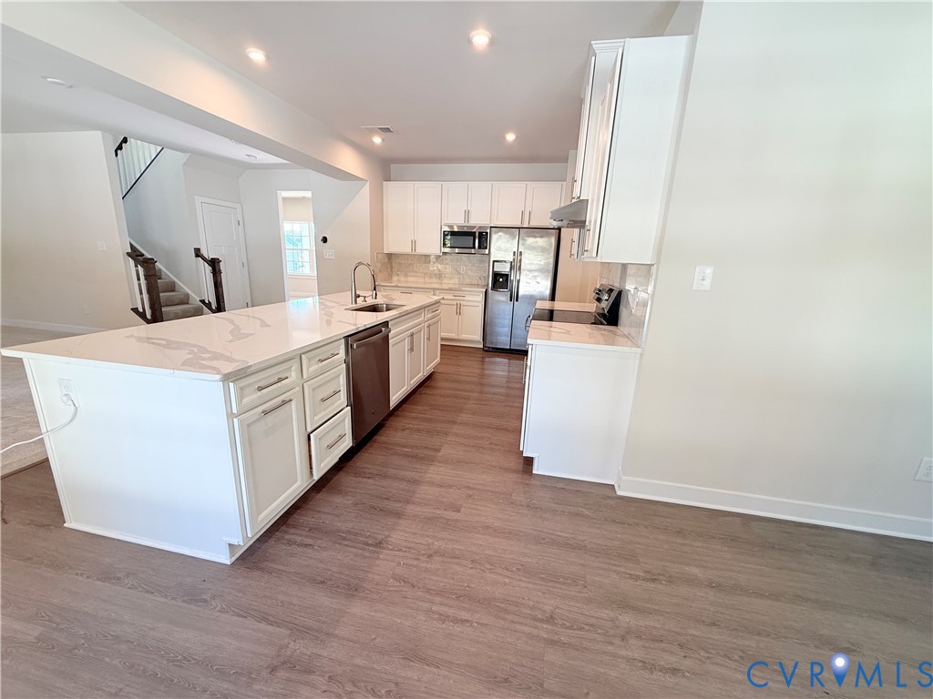 Kitchen featuring white shaker-style cabinetry, a quartz waterfall island, stainless steel appliances, and wood-finish flooring