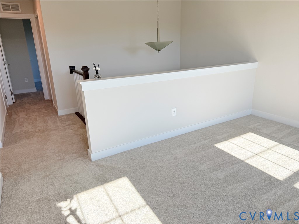 Neutral-toned carpeting, half-wall partition with a white cap, pendant lighting fixture, and a wooden handrail with balusters