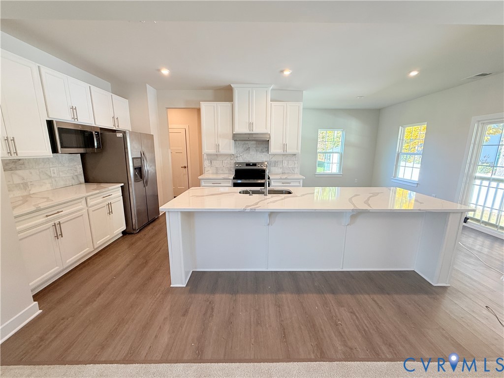 Kitchen featuring a large central island with a quartz countertop, white Shaker-style cabinetry, stainless steel appliances, tile backsplash, and wood-finish flooring