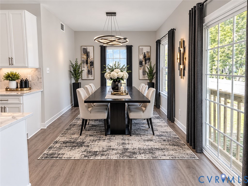 Virtually Staged Dining area featuring wood-finish flooring, a modern multi-ring chandelier, glass sliding doors with grid detailing, and recessed under-cabinet lighting