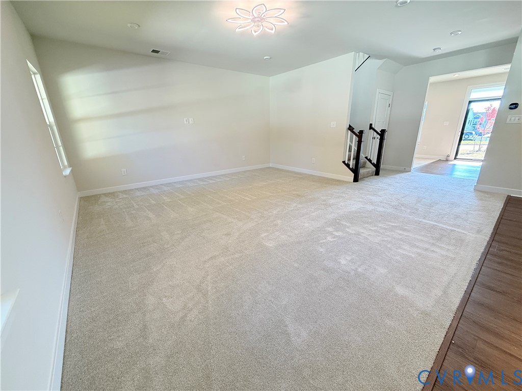 Interior space featuring neutral wall-to-wall carpeting, wood-finish flooring accents, recessed ceiling lighting, a decorative flush-mount light fixture, and a staircase with a dark-finish wooden railing