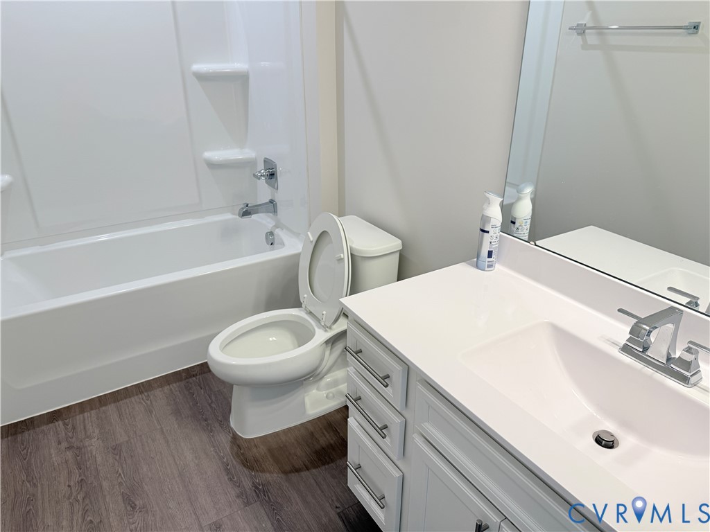Bathroom featuring a white vanity with a composite countertop and integrated basin, wood-finish flooring, and a tub-shower combination with a surround