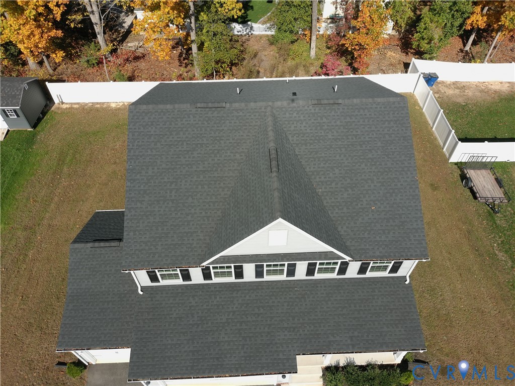 Aerial perspective featuring an asphalt shingle roof, gabled roofline, detached storage shed, and perimeter vinyl fencing