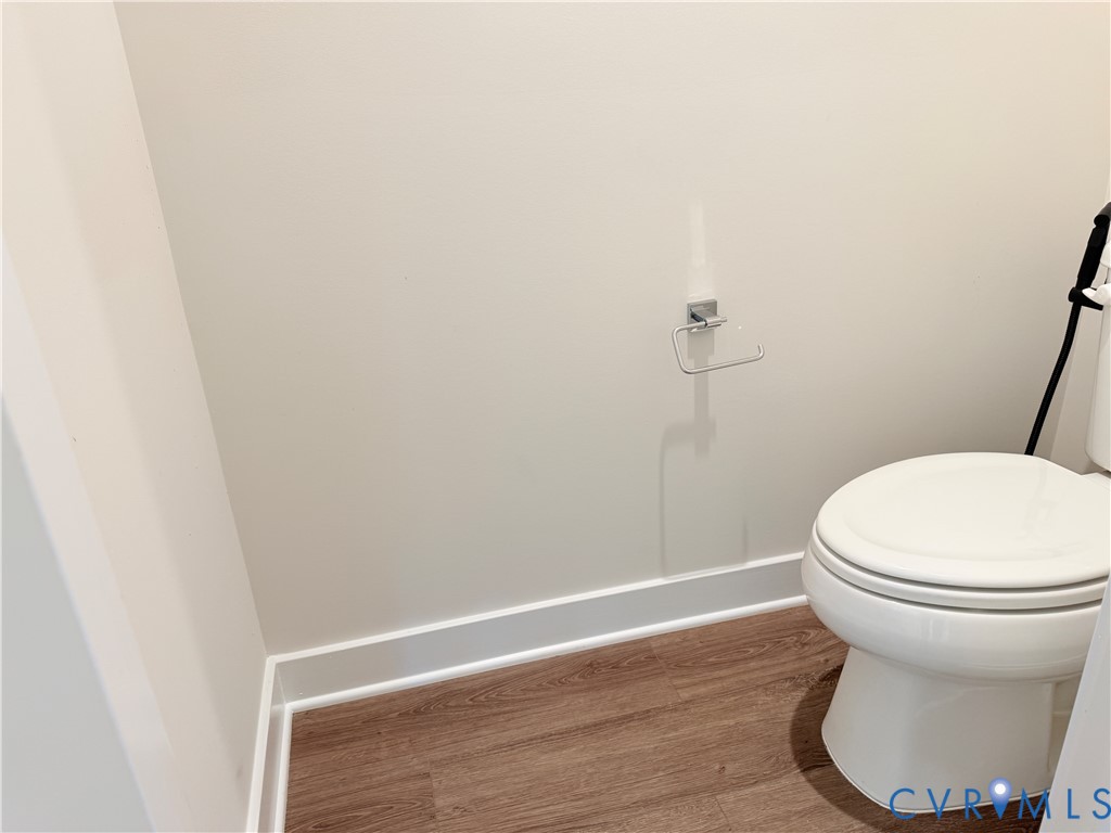 White porcelain toilet, wood-finish flooring, and chrome hardware