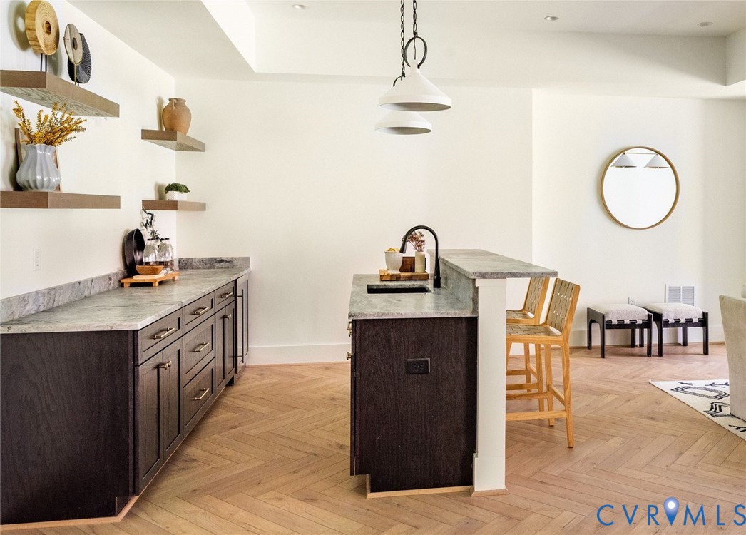 Lower level kitchenette with wine fridge, custom cabinetry, herringbone floors, island with seating, open to dining area.