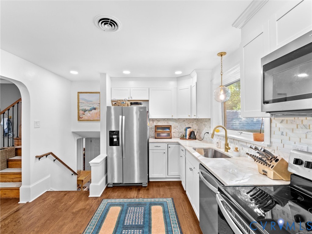 Kitchen featuring white shaker-style cabinetry, stone-finish countertops, stainless steel appliances, a brass-tone gooseneck faucet, and wood-finish flooring