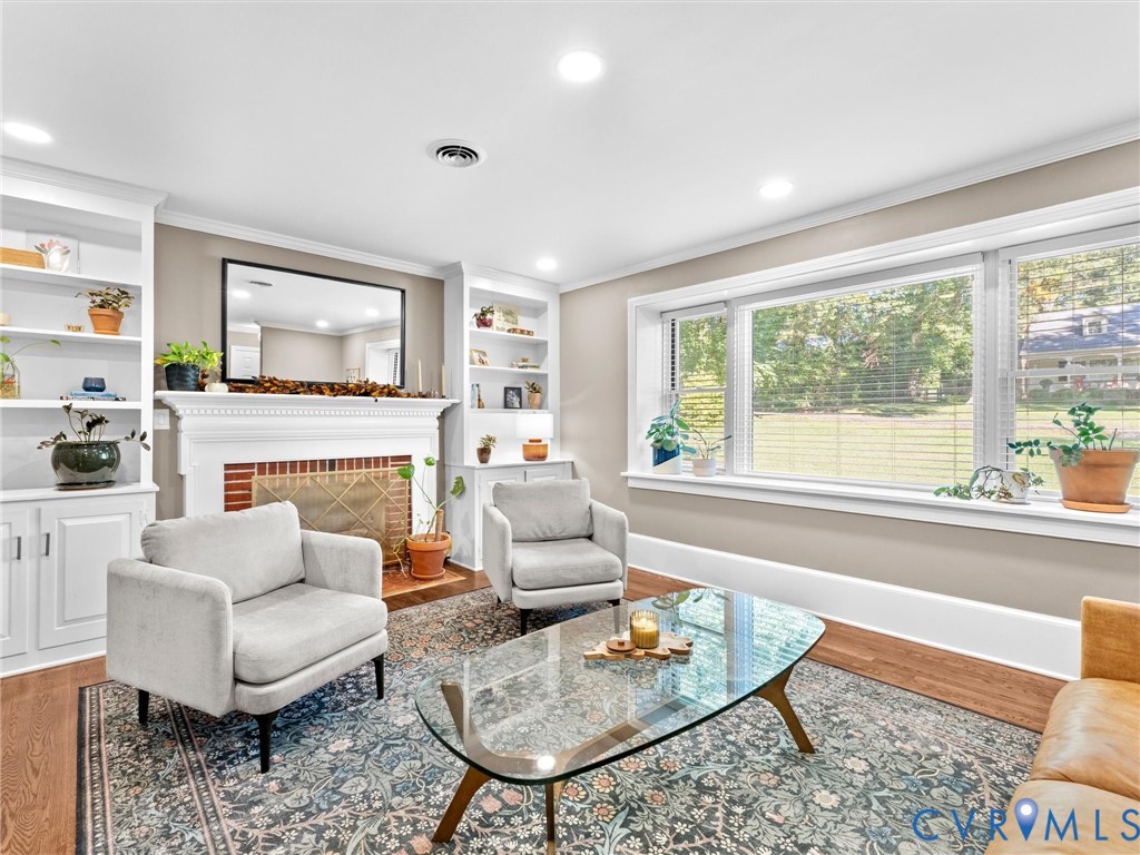 Living area featuring a brick-surround fireplace with a white mantel, built-in shelving, expansive picture window, recessed lighting, and wood-finish flooring