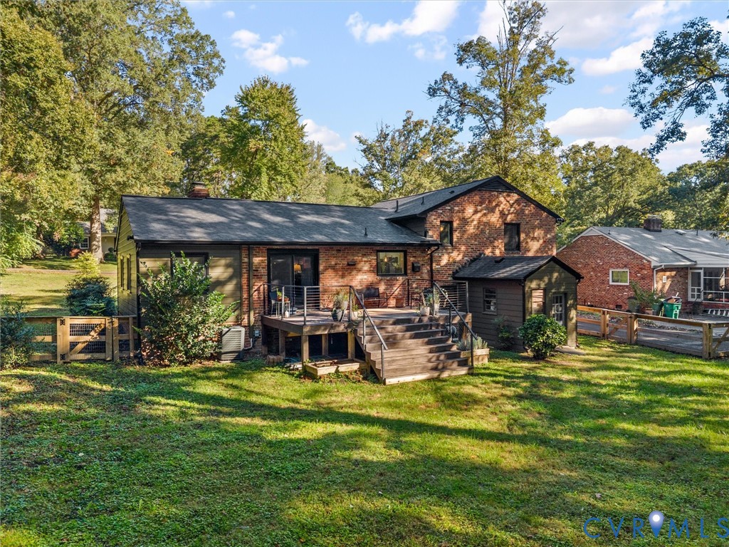 Brick exterior featuring an elevated wood deck with metal railings, a ground-level outbuilding, and wood-panel perimeter fencing surrounded by mature trees Brick exterior featuring an elevated wood deck with metal railings, a ground-level outbuilding, and wood-panel perimeter fencing surrounded by mature trees