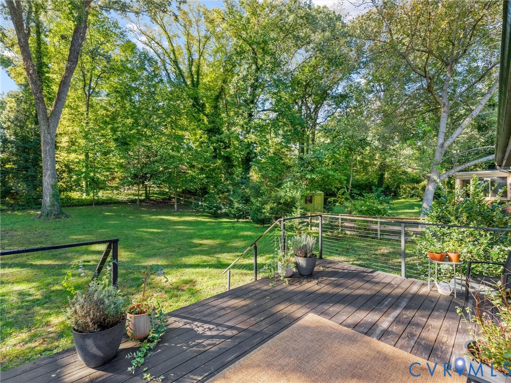 Raised deck featuring horizontal cable railing, wood-tone decking, and an expansive lawn with mature trees