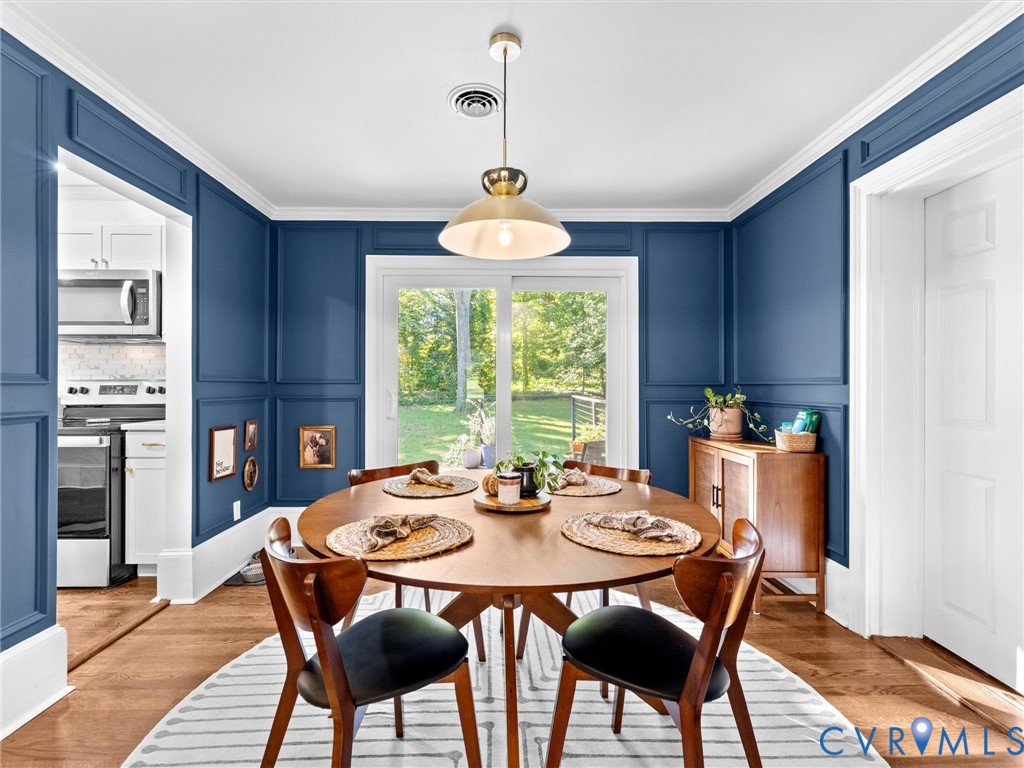 Dining area featuring decorative wall molding, hardwood flooring, a central pendant light fixture, and sliding glass doors
