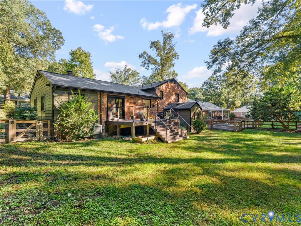Rear exterior featuring a multi-level wood deck, brick and horizontal siding facade, metal railing, and a fenced yard with mature trees