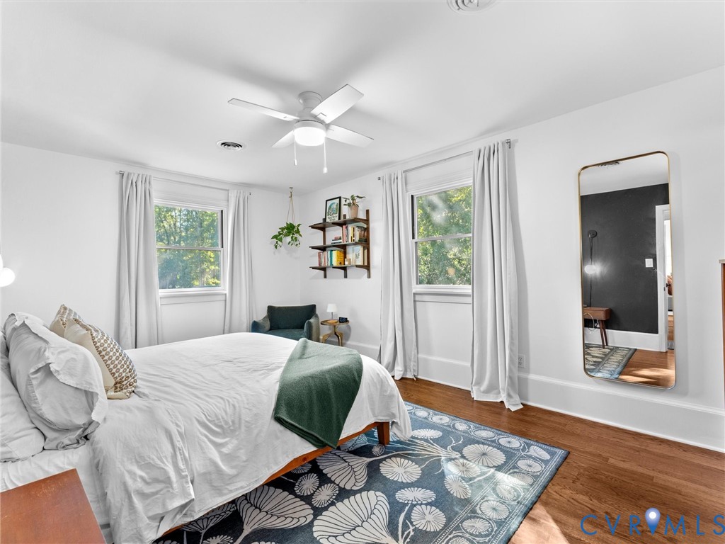 Wood-finish flooring, dual windows with white casing, and a central ceiling fan with integrated lighting