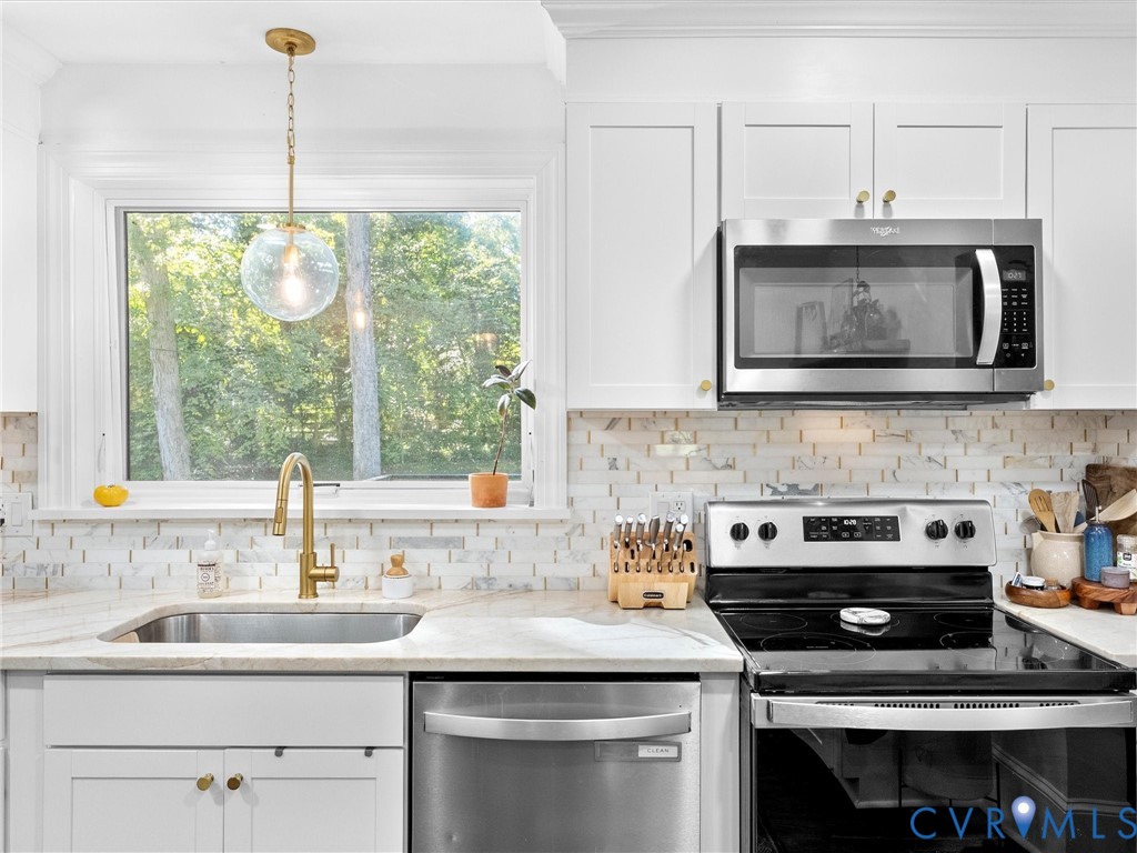 White cabinetry featuring brass hardware, brick-pattern backsplash, stainless steel appliances, brass pull-down faucet, and a globe-style pendant light