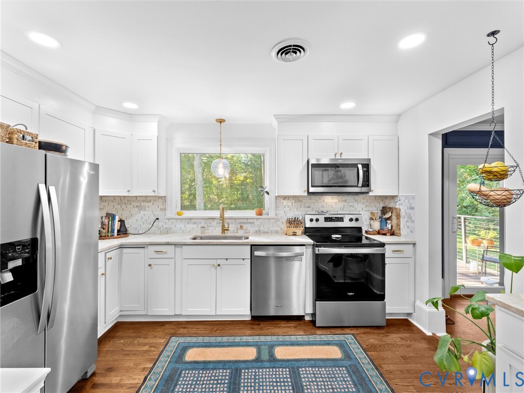Kitchen featuring white shaker-style cabinetry, stainless steel appliances, a mosaic tile backsplash, wood-finish flooring, and a window over the sink
