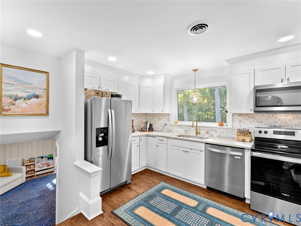 Kitchen featuring white shaker-style cabinetry, stainless steel appliances, a light-toned tile backsplash, and wood-finish flooring