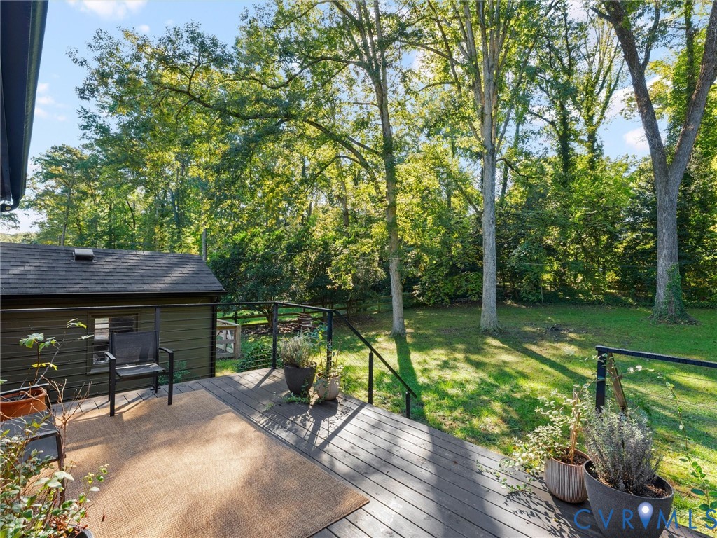 Elevated wood-plank deck featuring a black metal railing and expansive rear yard with mature trees