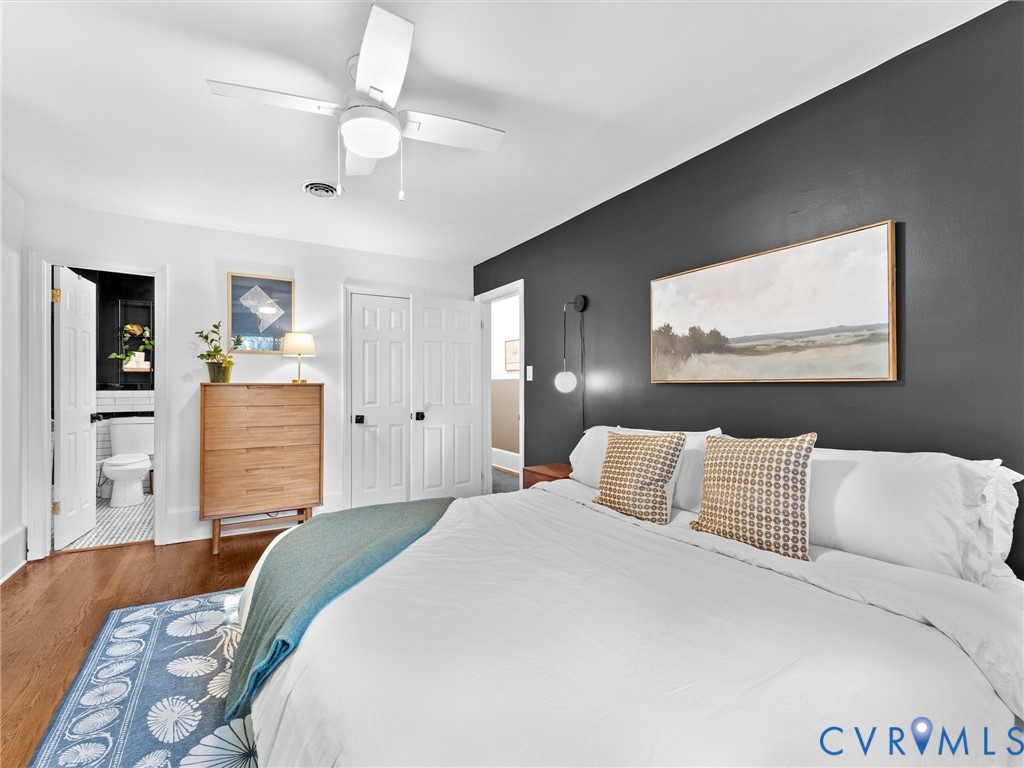 Bedroom featuring wood-finish flooring, a matte dark accent wall, white-paneled closet doors, and a ceiling-mounted light fixture with an integrated fan