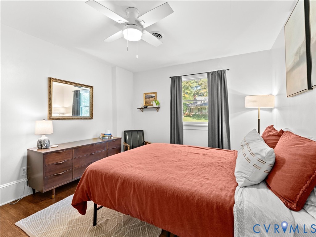 Neutral-toned room featuring wood-finish flooring, a white ceiling fan with integrated lighting, and a single-pane window with architectural trim