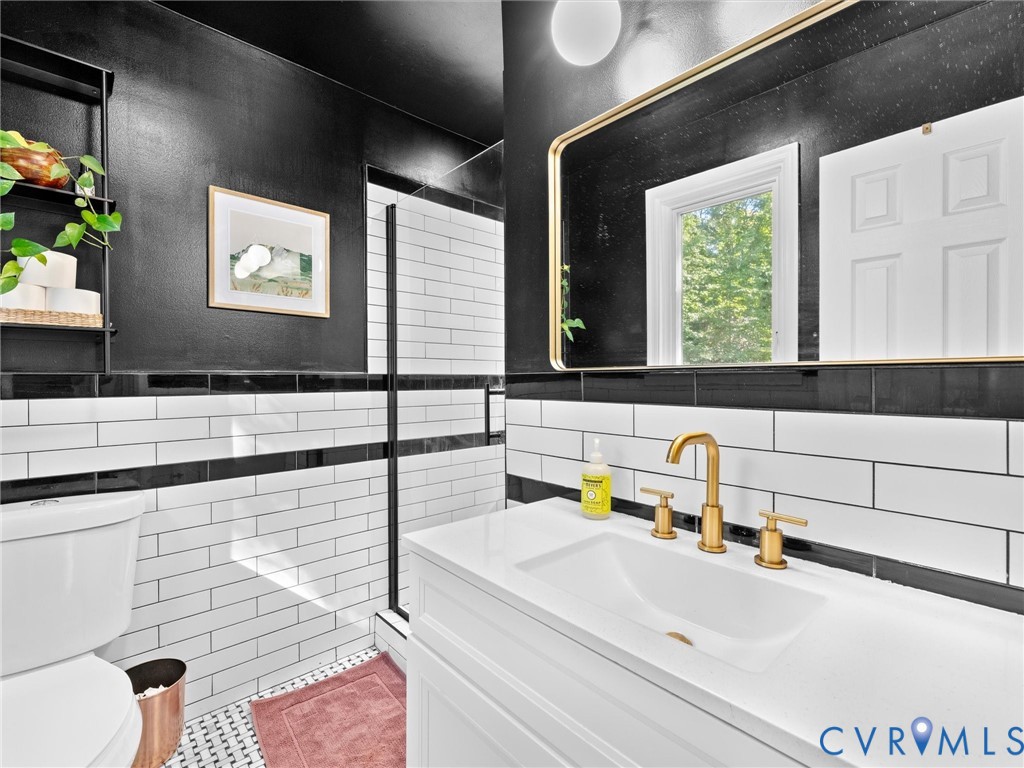 White vanity with a rectangular sink, brushed gold widespread faucet, rectangular mirror with metallic framing, and white and black subway tile wainscoting