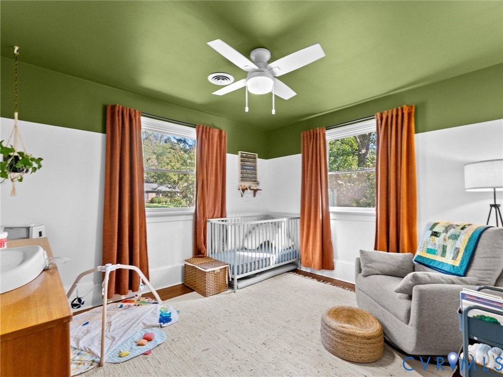 Bedroom featuring two double-hung windows, wood-finish flooring, and a white ceiling fan with integrated lighting