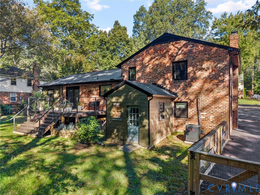 Brick Colonial home featuring a covered front porch with wooden railings, expansive rear deck with multi-level wooden construction, mature landscaping with established trees throughout the grounds, and a detached outbuilding Brick Colonial home featuring a covered front porch with wooden railings, expansive rear deck with multi-level wooden construction, mature landscaping with established trees throughout the grounds, and a detached outbuilding