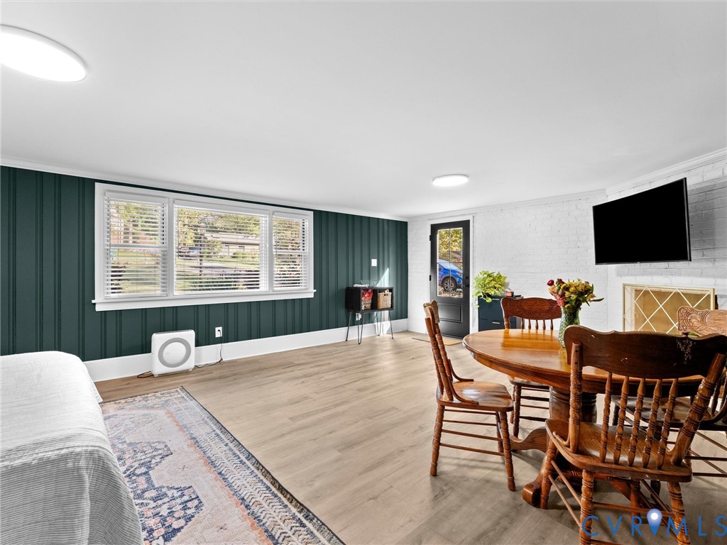 Interior space featuring wood-finish flooring, vertical paneling, large picture windows, a painted brick fireplace, and a glass-paneled exterior door
