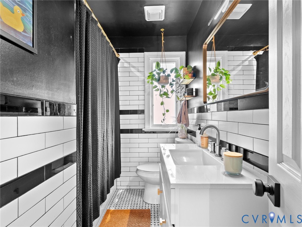 Bathroom featuring white subway tile walls with black accent banding, a floating white vanity with an integrated basin, a gold-framed rectangular mirror, and mosaic tile flooring