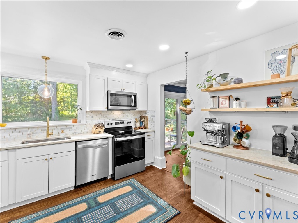 Kitchen featuring white cabinetry, wood-finish flooring, stainless steel appliances, light-toned countertops, and floating wood shelving