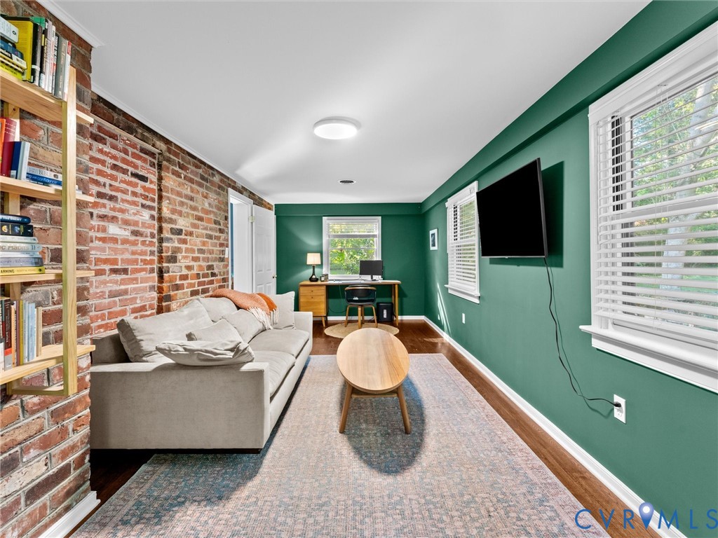 Exposed brick wall, wood-finish flooring, and multiple windows with horizontal blinds