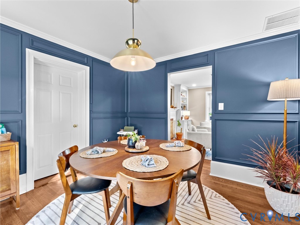 Dining space featuring deep blue wall paneling, crown molding, wood-finish flooring, and a brass-tone pendant light fixture