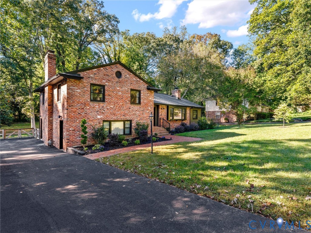 Two-story brick exterior featuring a chimney, asphalt driveway, brick walkway, and mature landscaping