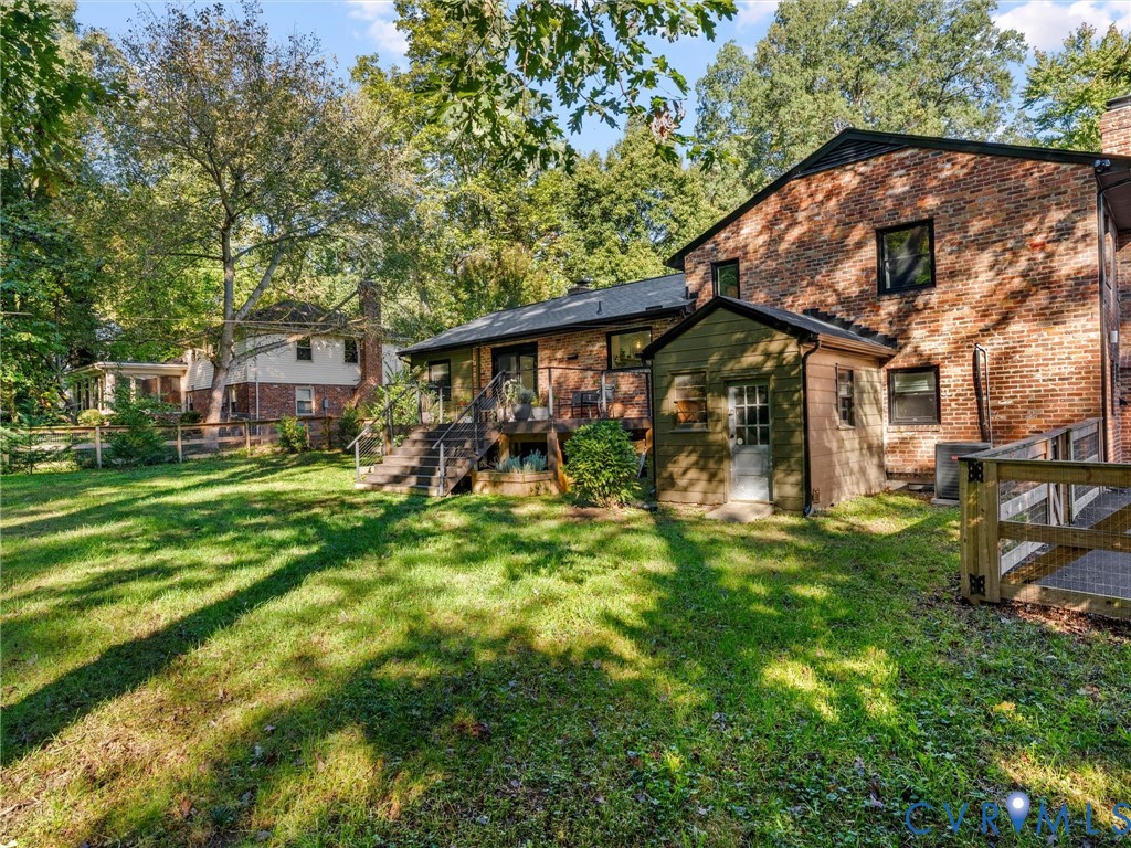 Brick exterior featuring a multi-level wood deck, side addition, and mature trees on a level lot