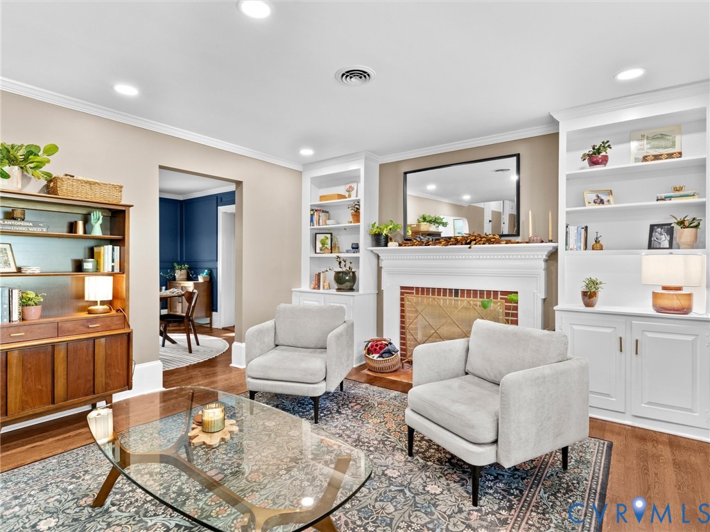 Living area featuring a fireplace with brick surround, built-in cabinetry, recessed lighting, and wood-finish flooring