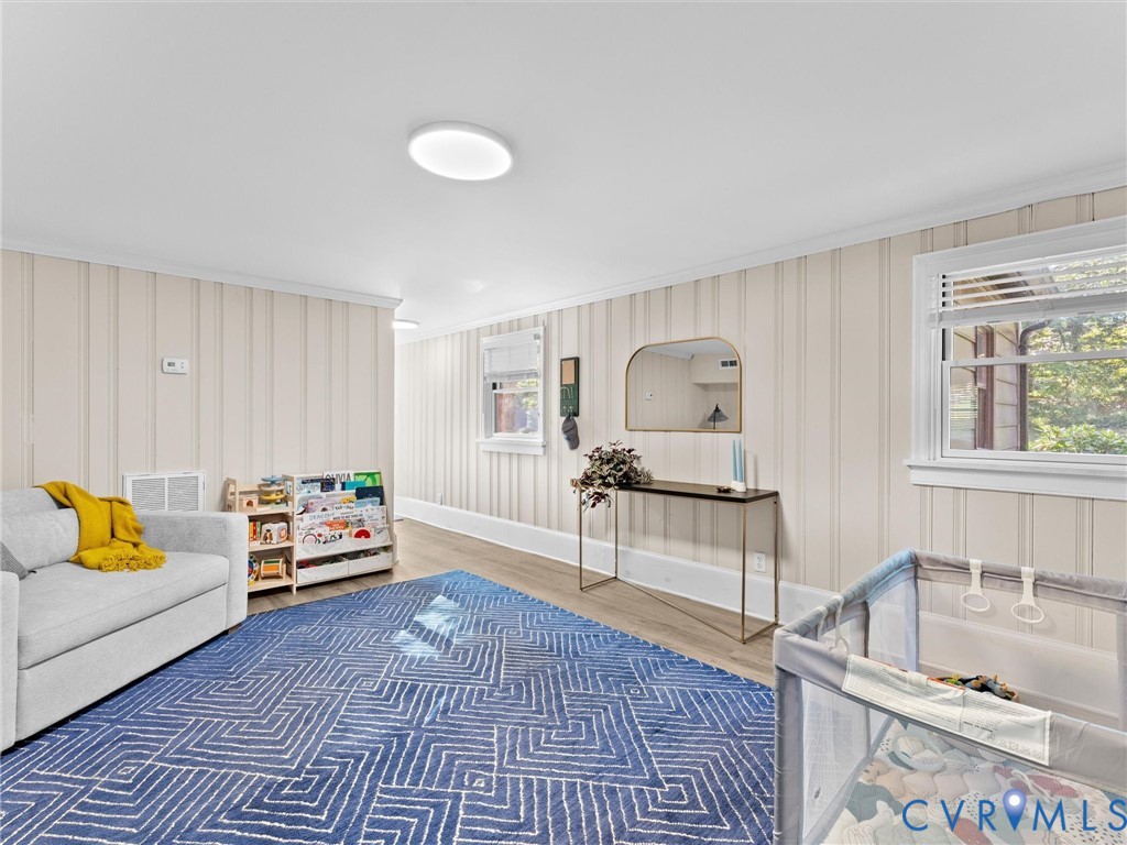 Interior space featuring vertical wood-plank wall paneling, light-tone wood-finish flooring, two double-hung windows, and flush-mount circular overhead lighting
